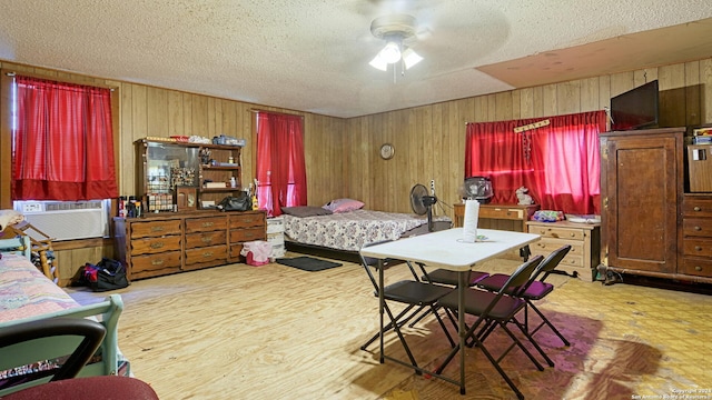 bedroom featuring wood walls, light hardwood / wood-style floors, ceiling fan, and a textured ceiling