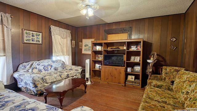 sitting room with a textured ceiling, wood-type flooring, wood walls, and ceiling fan