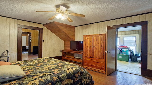 bedroom with ceiling fan, wood walls, a textured ceiling, light wood-type flooring, and crown molding