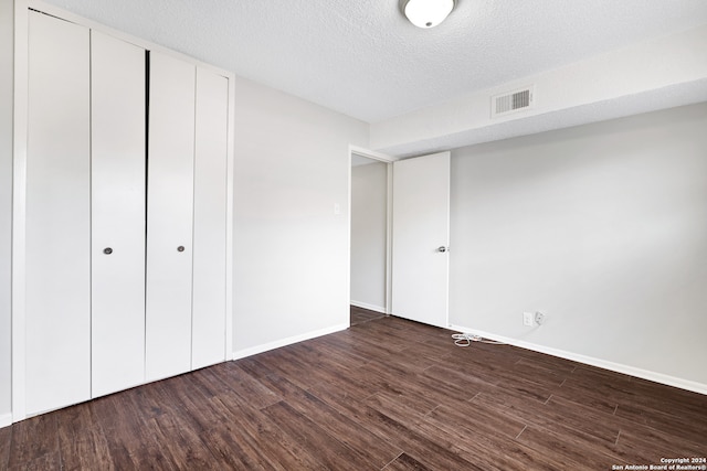 unfurnished bedroom with a textured ceiling, dark hardwood / wood-style floors, and a closet