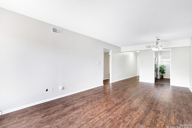 unfurnished room featuring a textured ceiling, a notable chandelier, and dark hardwood / wood-style flooring