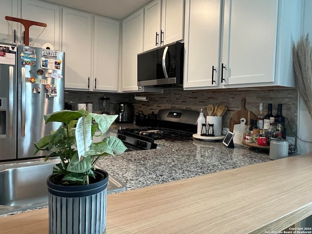 kitchen with light wood-type flooring, white cabinets, stainless steel appliances, and dark stone counters