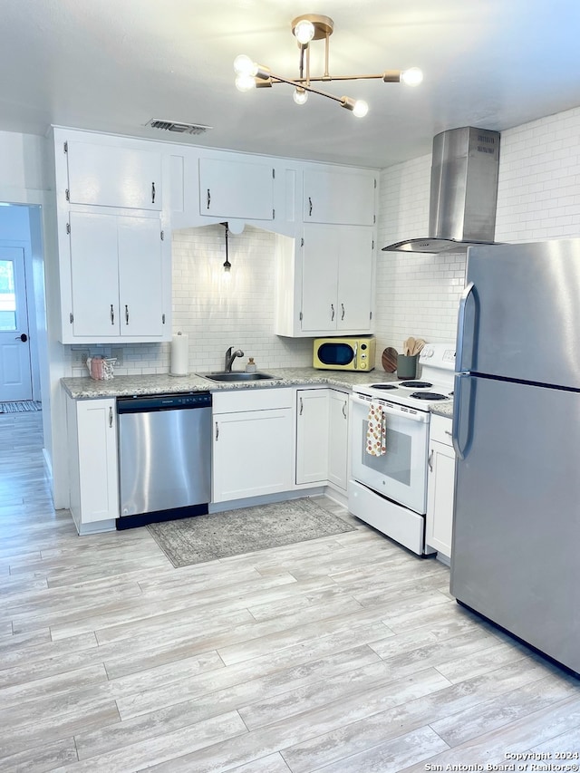 kitchen with stainless steel appliances, wall chimney exhaust hood, white cabinets, and light hardwood / wood-style floors