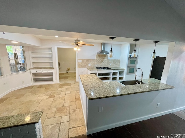 kitchen with hanging light fixtures, sink, wall chimney exhaust hood, and dark stone counters