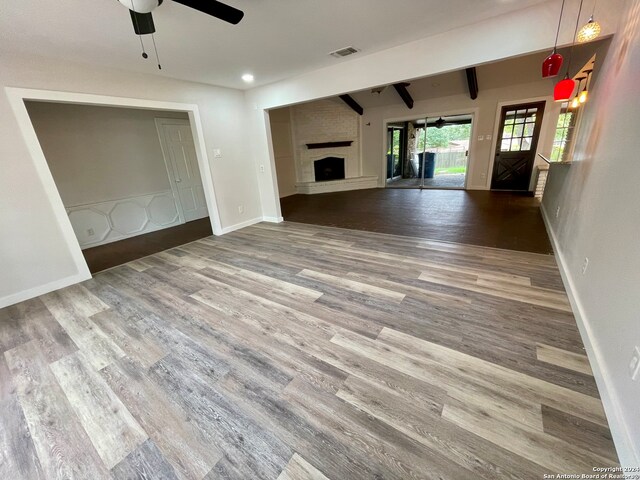 unfurnished living room featuring a large fireplace, ceiling fan, hardwood / wood-style flooring, and beam ceiling