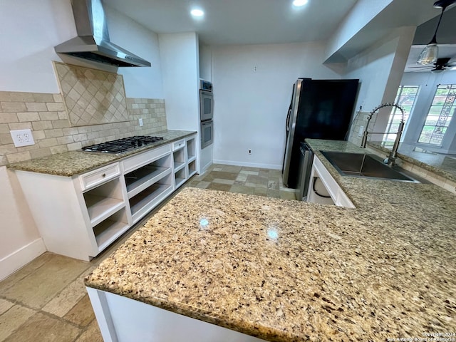 kitchen featuring white cabinetry, sink, wall chimney range hood, ceiling fan, and pendant lighting