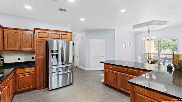 kitchen featuring stainless steel fridge with ice dispenser, an inviting chandelier, backsplash, decorative light fixtures, and dark stone countertops