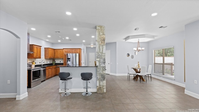 kitchen featuring sink, a notable chandelier, wall chimney range hood, stainless steel appliances, and light tile patterned floors