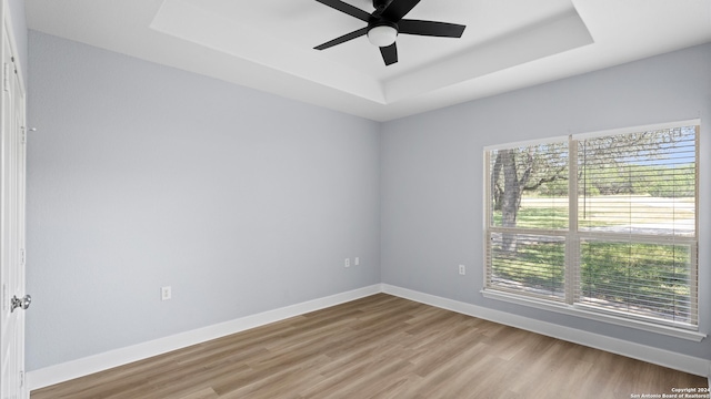 empty room with a healthy amount of sunlight, hardwood / wood-style floors, ceiling fan, and a raised ceiling