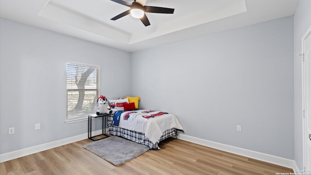 bedroom featuring a raised ceiling, light hardwood / wood-style floors, and ceiling fan