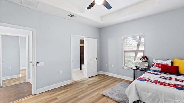 bedroom with ceiling fan, ensuite bathroom, light hardwood / wood-style flooring, and a raised ceiling