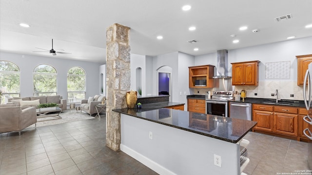 kitchen with ceiling fan, sink, wall chimney range hood, appliances with stainless steel finishes, and ornate columns