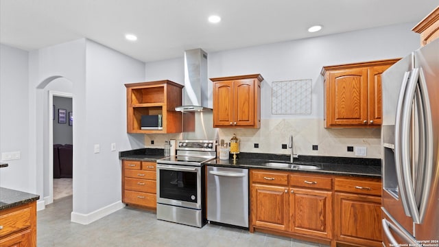 kitchen featuring appliances with stainless steel finishes, decorative backsplash, dark stone counters, sink, and wall chimney range hood