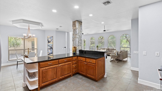 kitchen with dark stone counters, ceiling fan with notable chandelier, a textured ceiling, and decorative light fixtures