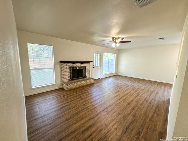 unfurnished living room featuring ceiling fan, a brick fireplace, and dark hardwood / wood-style flooring