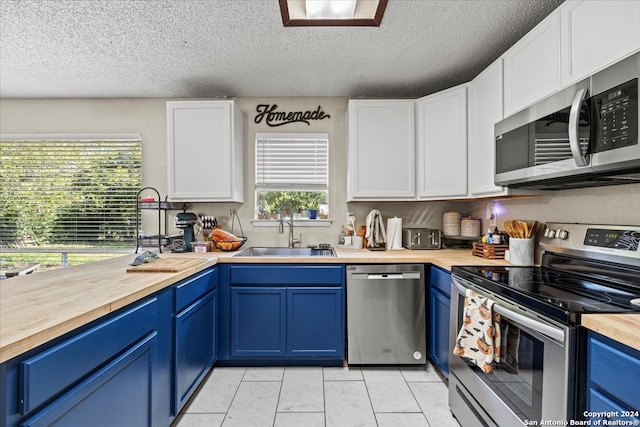 kitchen featuring blue cabinetry, wood counters, stainless steel appliances, sink, and white cabinetry