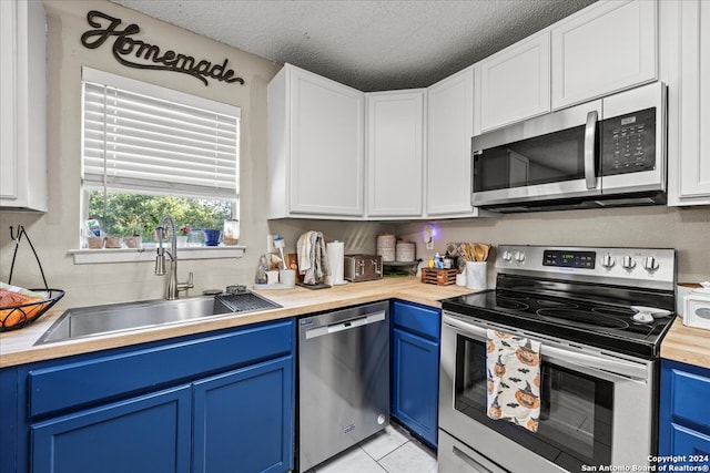 kitchen with blue cabinets, light tile patterned floors, stainless steel appliances, and white cabinets