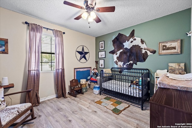 bedroom with a textured ceiling, ceiling fan, light wood-type flooring, and a crib