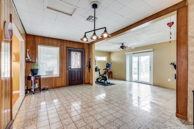 tiled entryway featuring ceiling fan and wooden walls