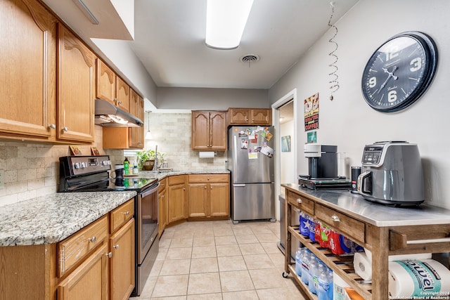 kitchen featuring light tile patterned floors, light stone counters, stainless steel appliances, and decorative backsplash