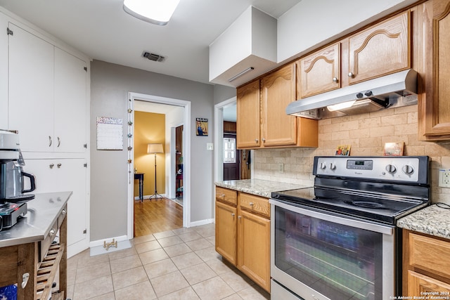 kitchen with light tile patterned floors, light stone countertops, backsplash, and stainless steel range with electric cooktop