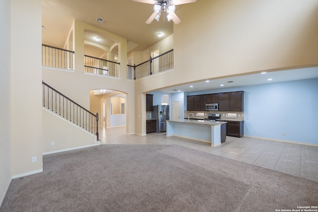 unfurnished living room with a towering ceiling, light colored carpet, sink, and ceiling fan