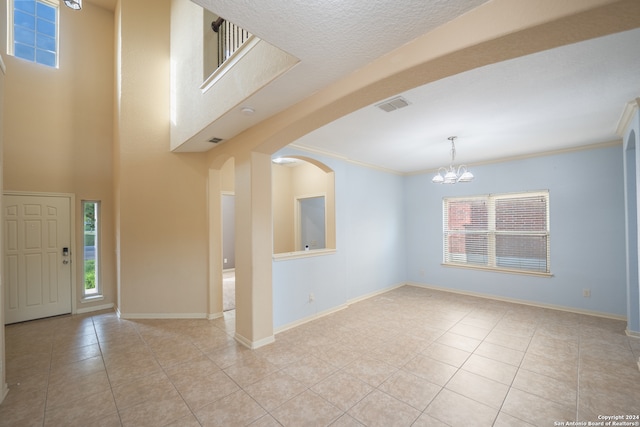 entryway with light tile patterned floors, an inviting chandelier, a textured ceiling, and ornamental molding