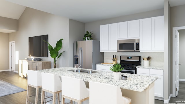 kitchen with an island with sink, wood-type flooring, stainless steel appliances, white cabinets, and light stone counters