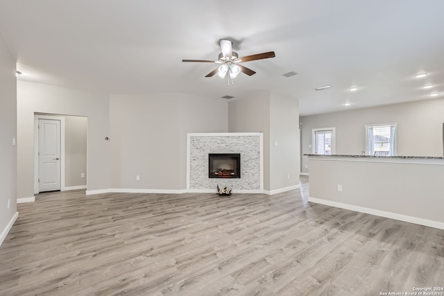 unfurnished living room featuring ceiling fan, a stone fireplace, and light wood-type flooring