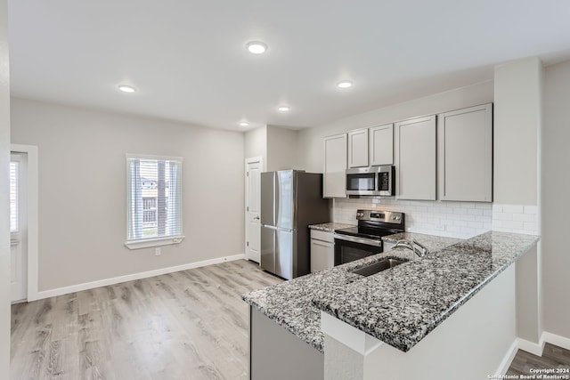 kitchen with appliances with stainless steel finishes, backsplash, kitchen peninsula, light wood-type flooring, and stone counters