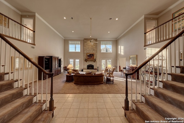 living room with ornamental molding, ceiling fan, a stone fireplace, a towering ceiling, and light colored carpet