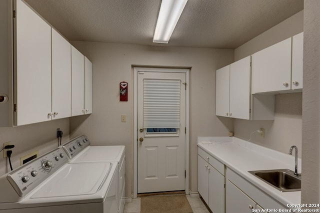 clothes washing area with light tile patterned floors, sink, washing machine and clothes dryer, cabinets, and a textured ceiling