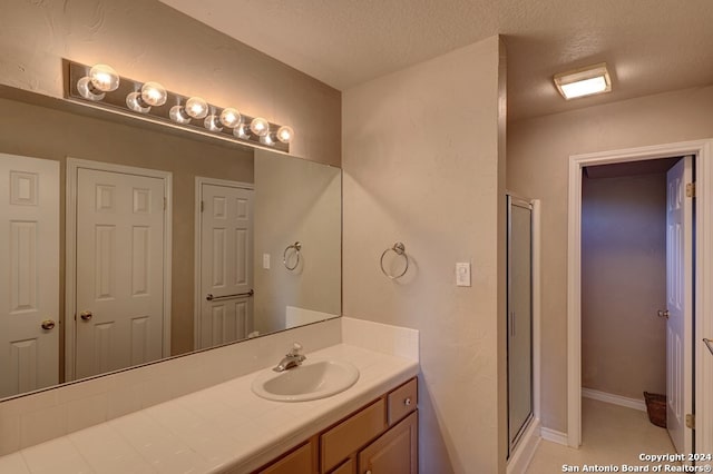 bathroom with vanity, a textured ceiling, and a shower with door