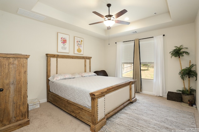 bedroom with ceiling fan, light carpet, and a tray ceiling