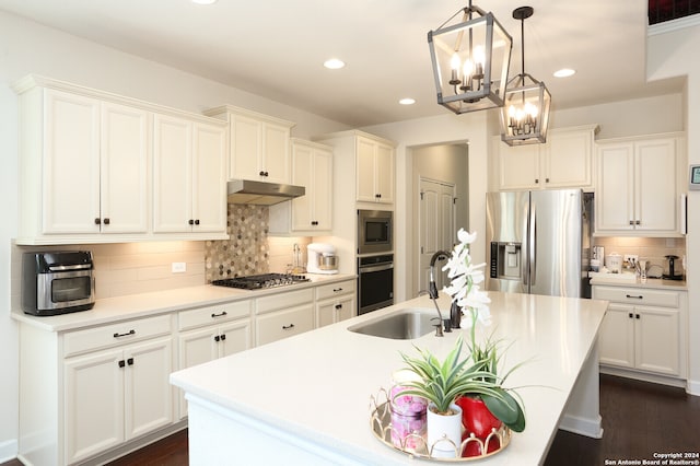 kitchen with an inviting chandelier, appliances with stainless steel finishes, dark hardwood / wood-style flooring, pendant lighting, and a kitchen island with sink