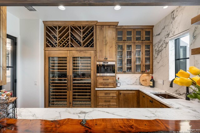 interior space featuring sink, light stone counters, wine cooler, and decorative backsplash