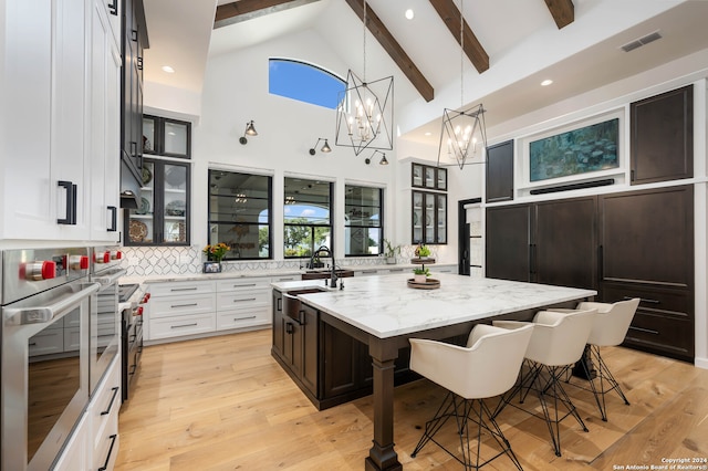 kitchen with oven, white cabinetry, sink, beam ceiling, and a kitchen island with sink