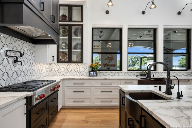 kitchen with stainless steel gas cooktop, light stone counters, white cabinetry, and light hardwood / wood-style floors