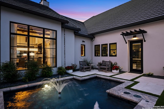 pool at dusk featuring pool water feature and a patio