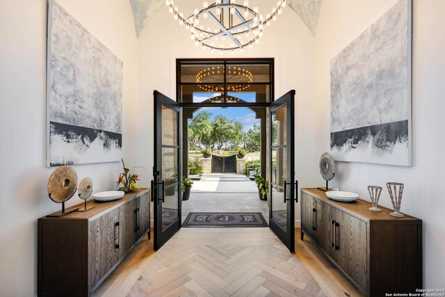 entryway with french doors, lofted ceiling, a notable chandelier, and light parquet flooring