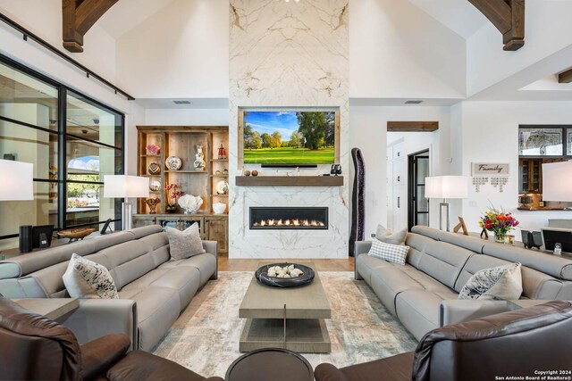 living room featuring light wood-type flooring, a premium fireplace, high vaulted ceiling, and beam ceiling