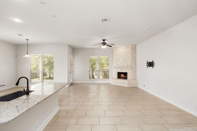 unfurnished living room with a stone fireplace, ceiling fan, and sink