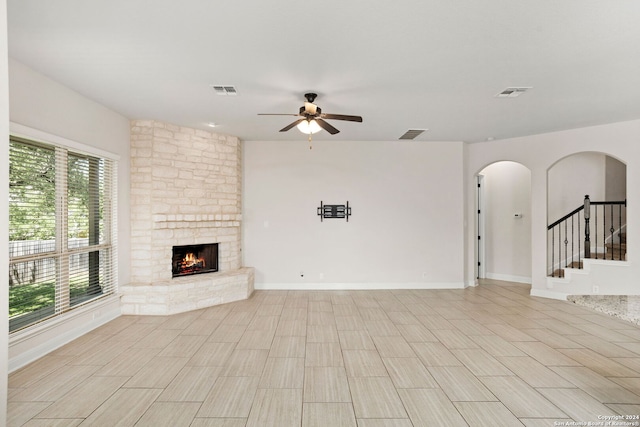 unfurnished living room with a stone fireplace, a wealth of natural light, and ceiling fan