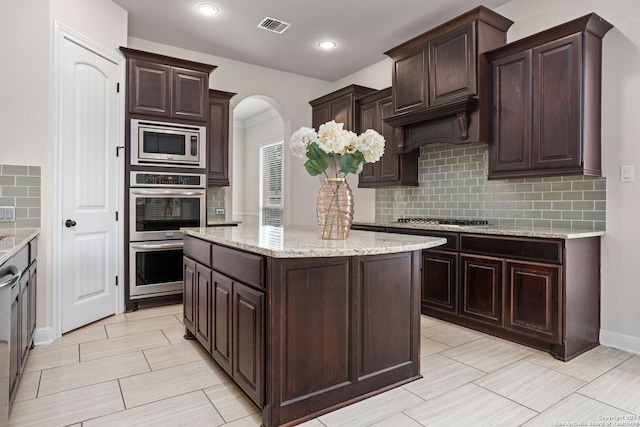 kitchen featuring tasteful backsplash, dark brown cabinetry, a kitchen island, and appliances with stainless steel finishes