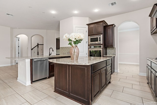 kitchen featuring dark brown cabinetry, decorative backsplash, a center island, and stainless steel appliances