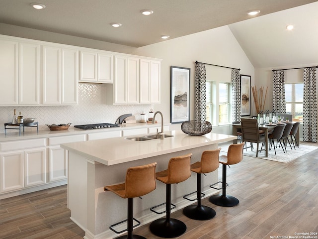 kitchen featuring vaulted ceiling, a center island with sink, stainless steel gas stovetop, white cabinets, and sink