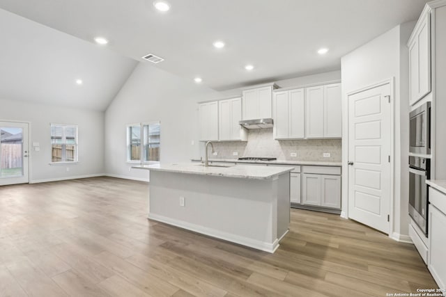 kitchen with vaulted ceiling, stainless steel appliances, a kitchen island with sink, white cabinetry, and sink