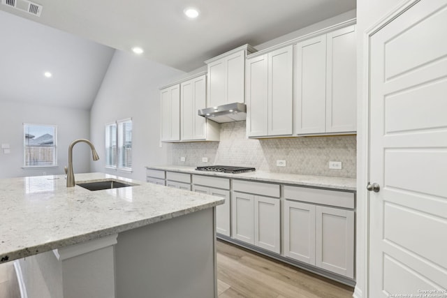 kitchen with white cabinets, stainless steel gas cooktop, light stone counters, sink, and lofted ceiling