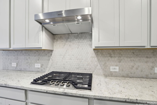 kitchen with light stone counters, white cabinets, stainless steel gas cooktop, and backsplash