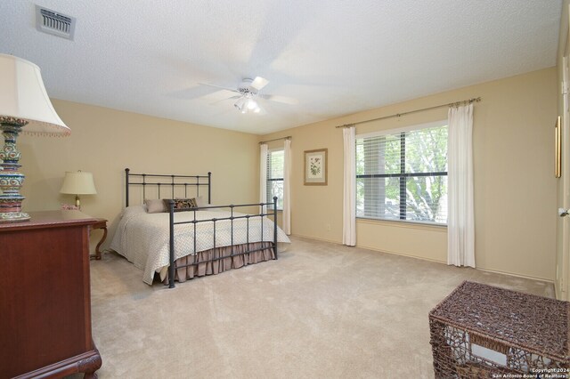 bedroom with ceiling fan, light carpet, and a textured ceiling